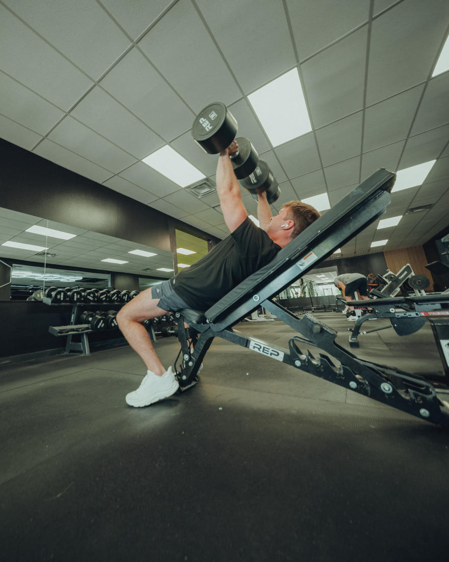 A member pressing dumbbells on an incline bench at The Forum